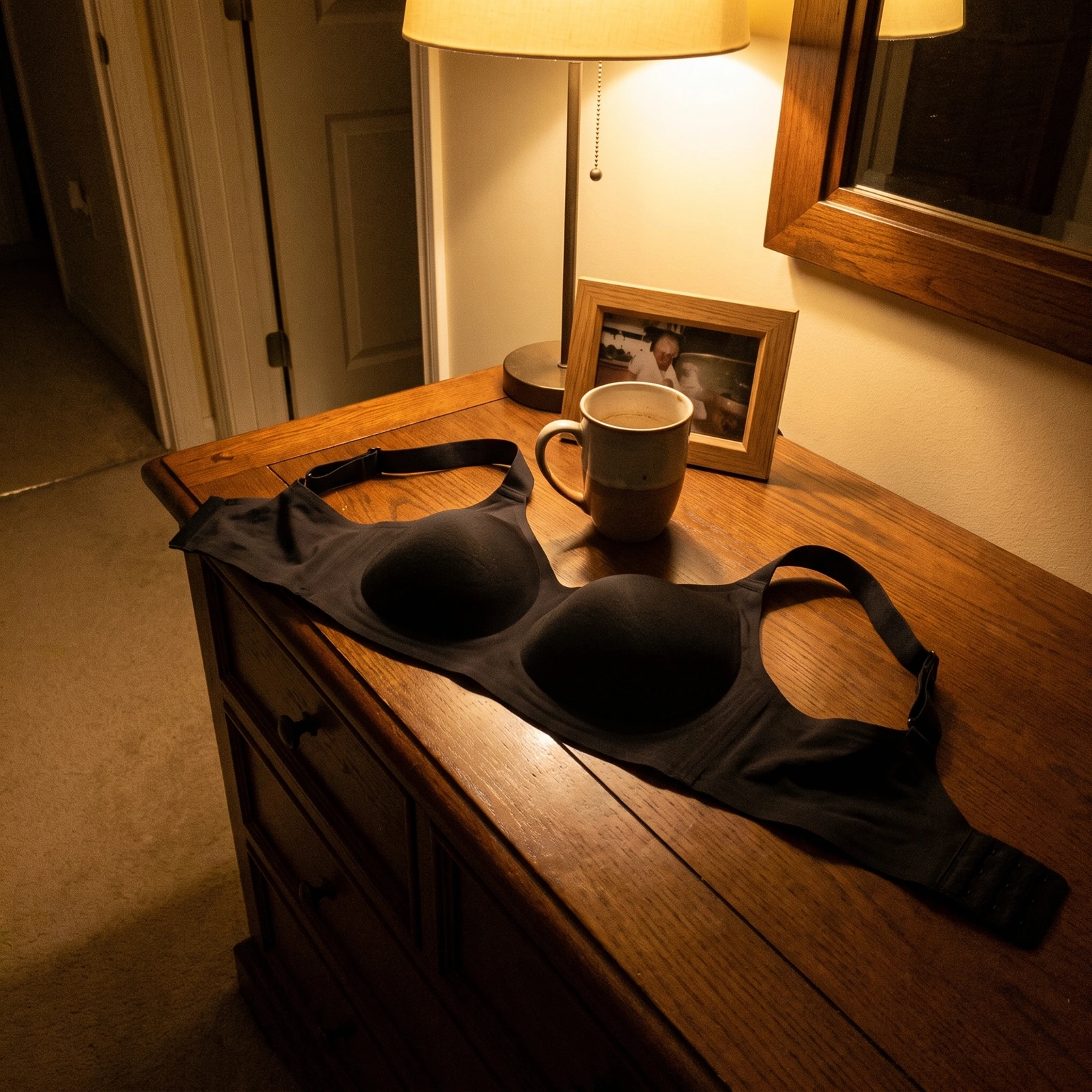 Le soutien-gorge noir posé sur une commode, le soir, près d'une lampe
